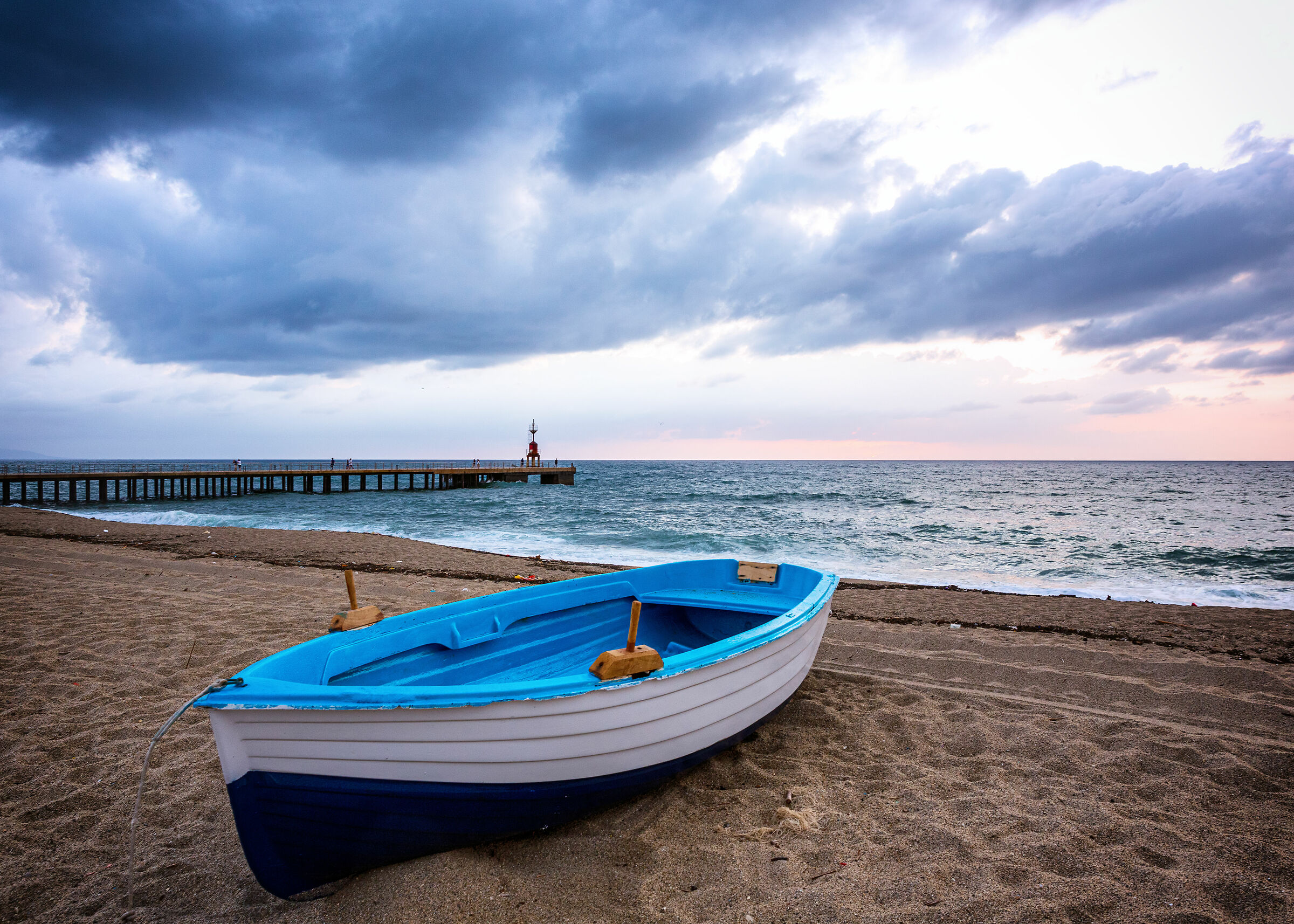 A boat, a jetty, a man, a seagull, the sea