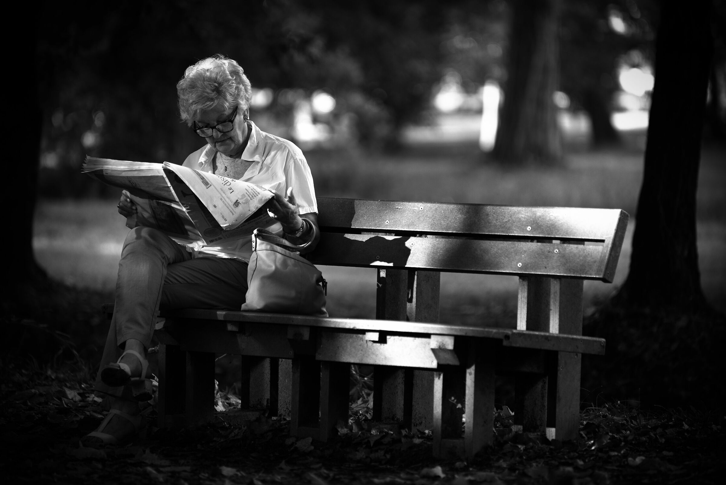 A grandni who reads the newspaper on the bench