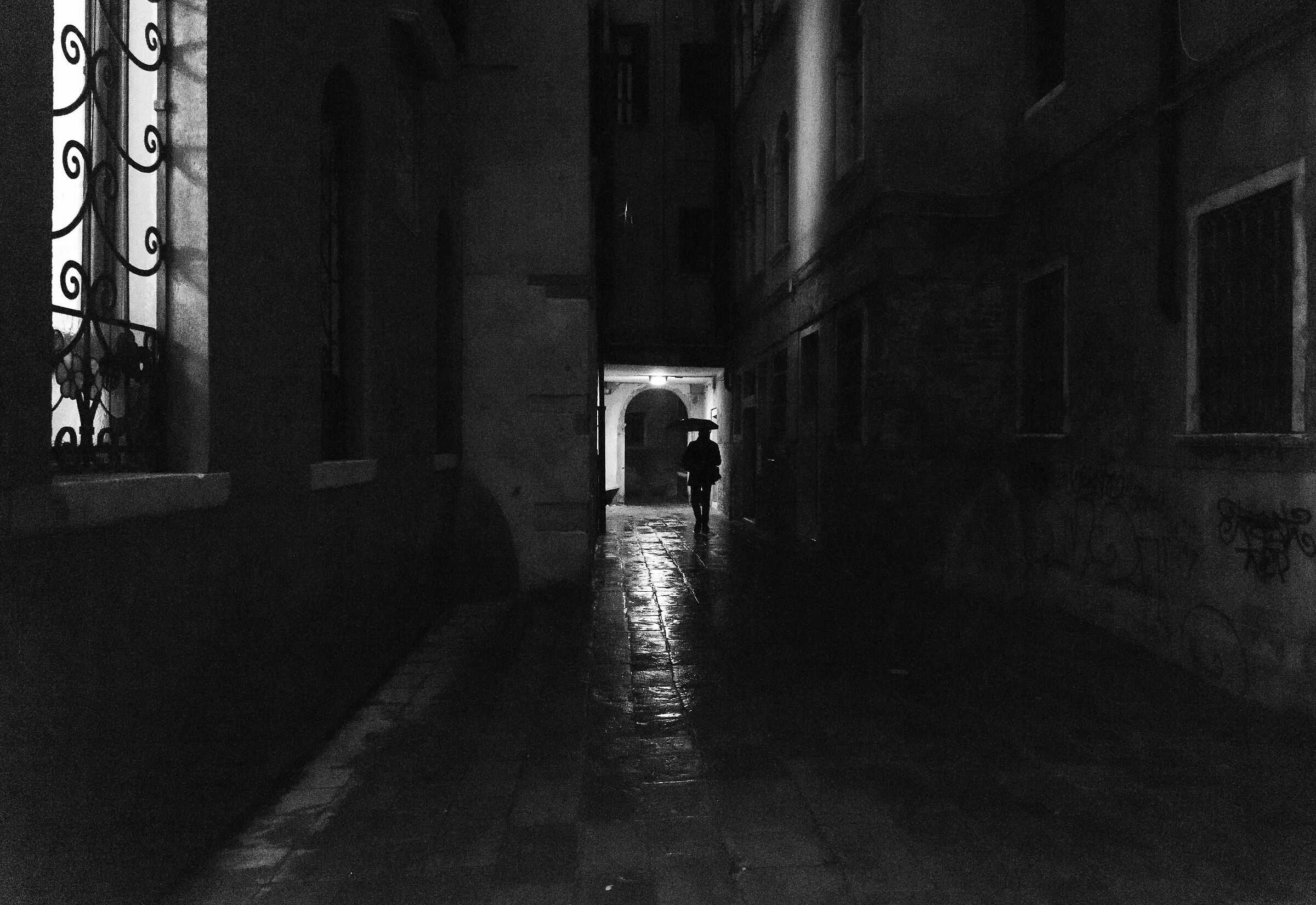 Solo, con l'ombrello, in una calle di ombre e luci