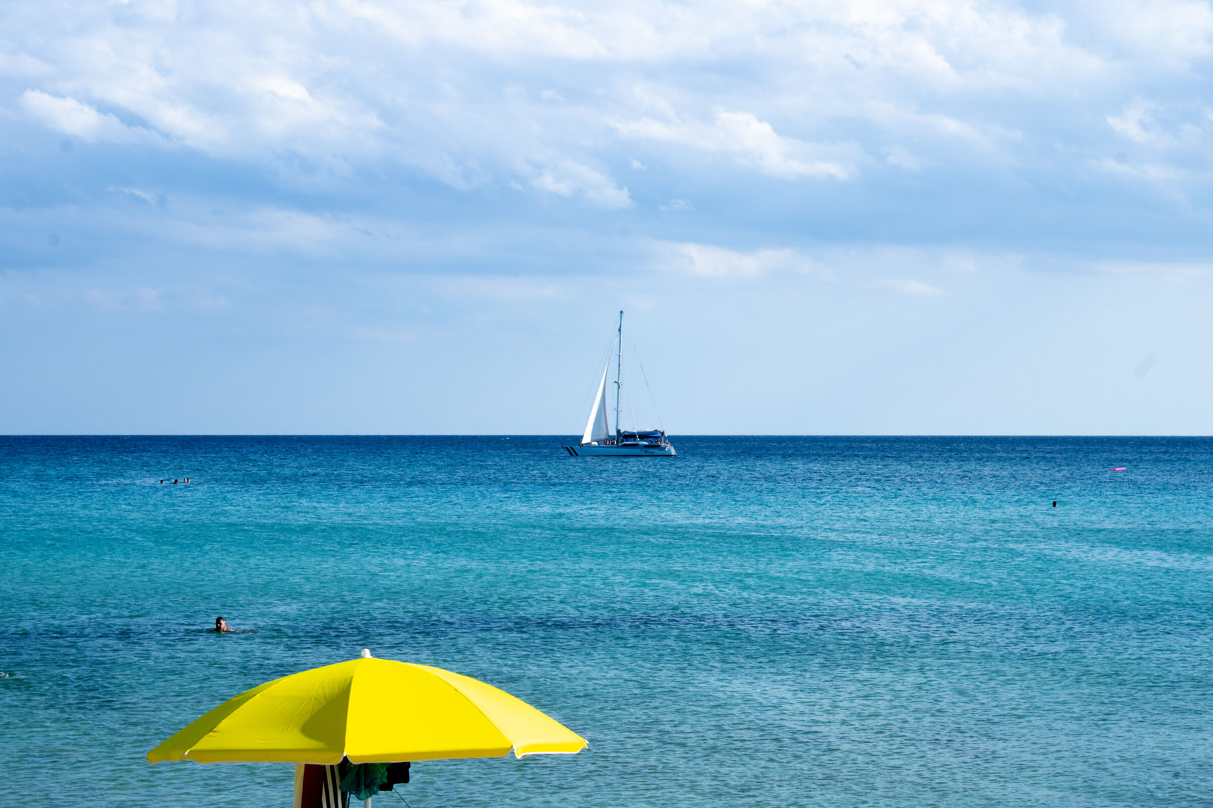 Mare con barca a vela e ombrellone giallo
