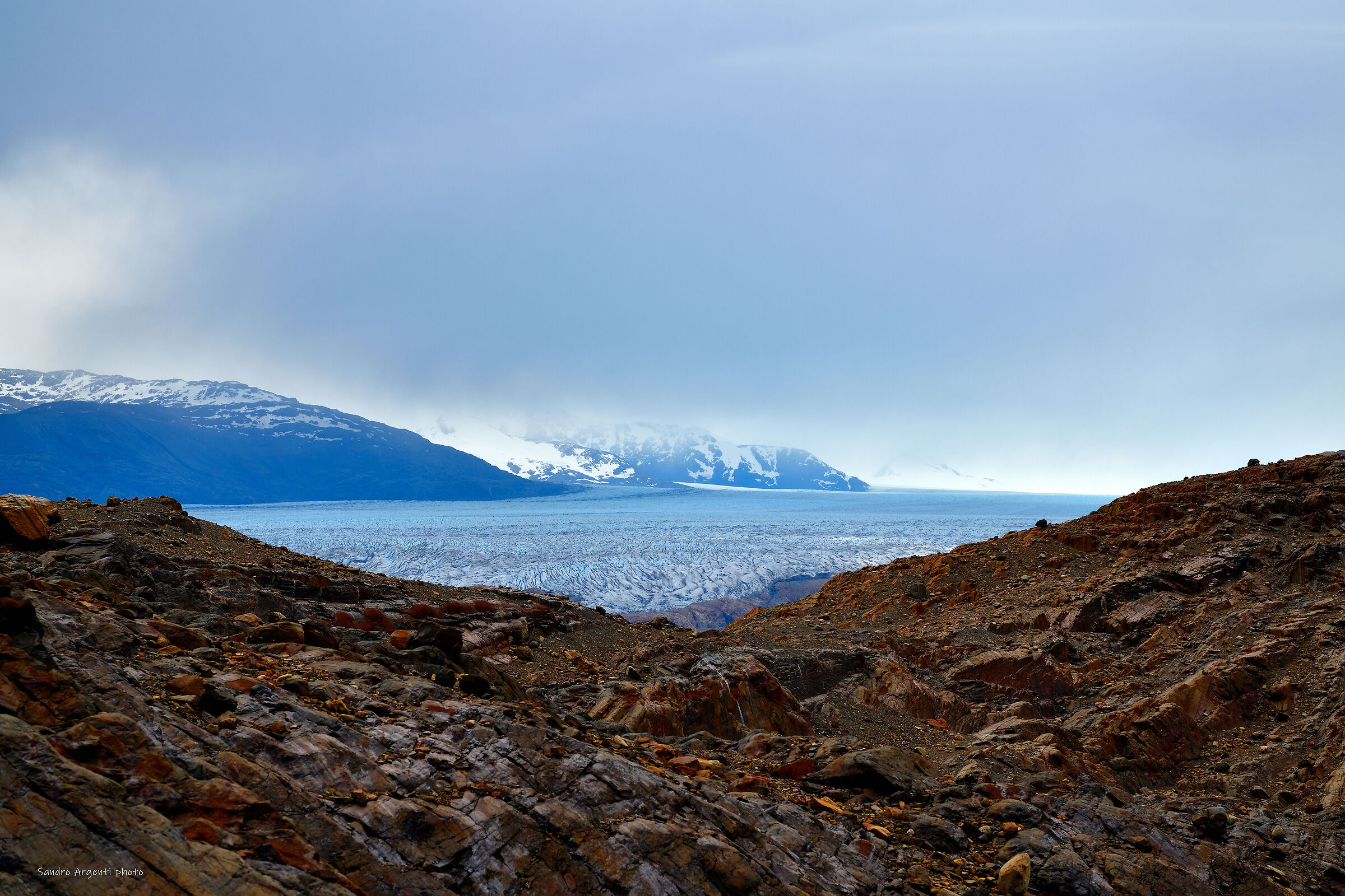 L'immenso ghiacciaio scorre fra nuvole e montagne.